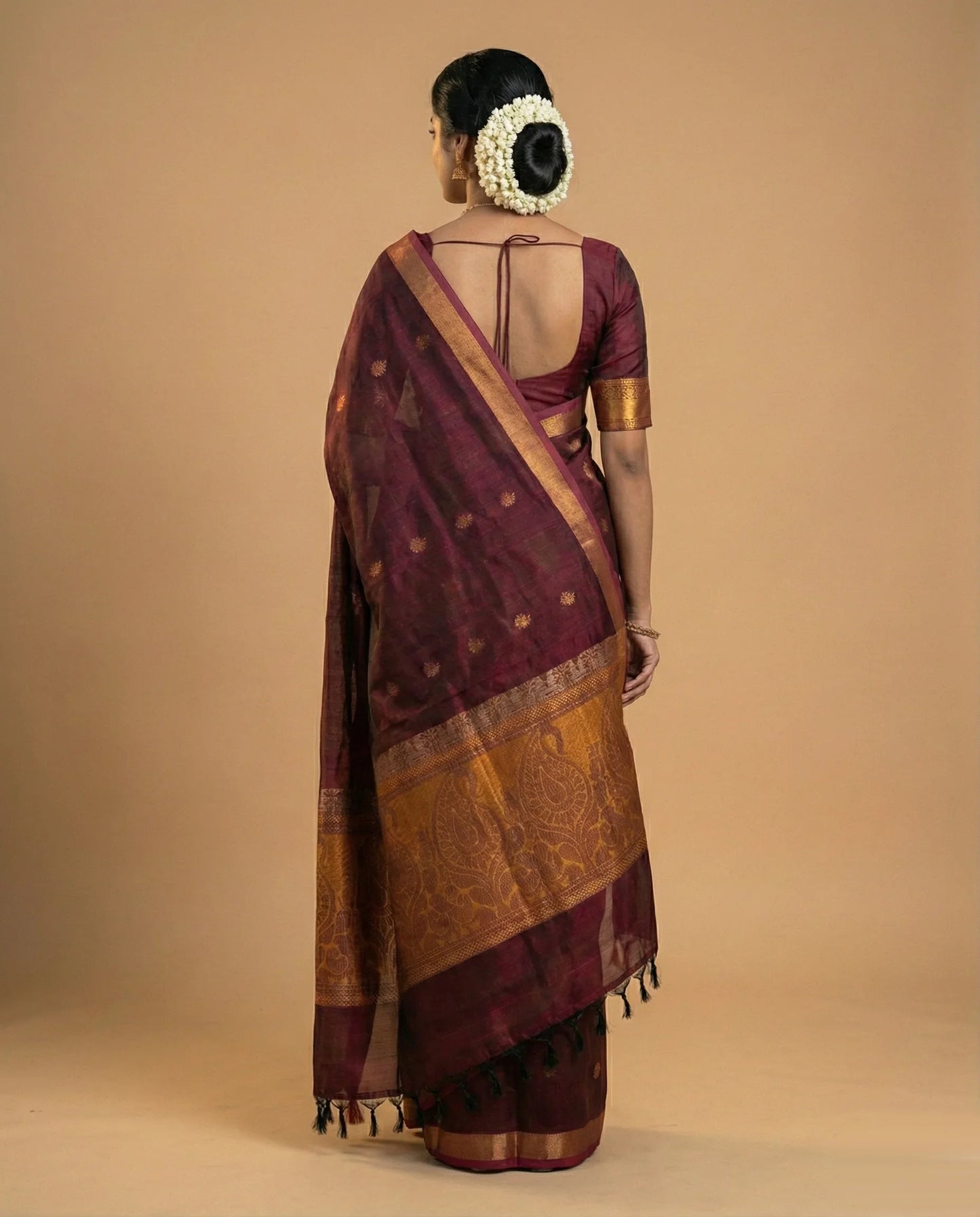Woman wearing a traditional maroon saree with gold border on a beige background