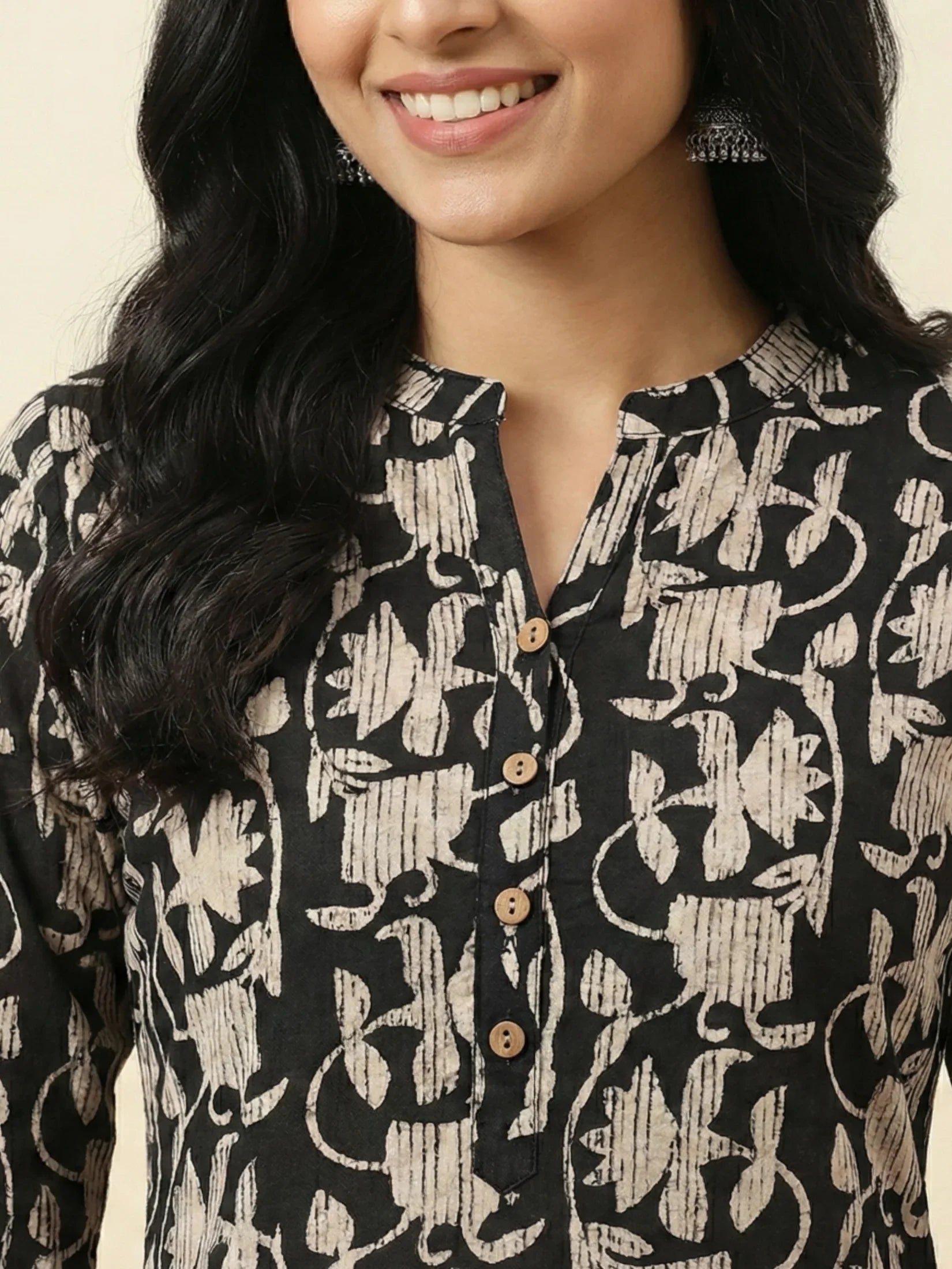 Woman wearing a black and white patterned blouse with a beige background.
