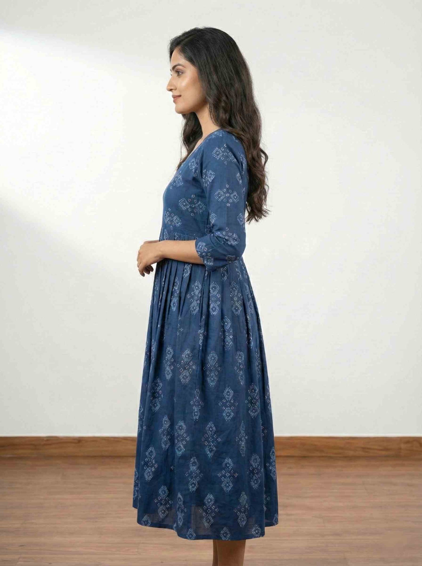 Woman wearing a blue patterned dress against a white wall.

