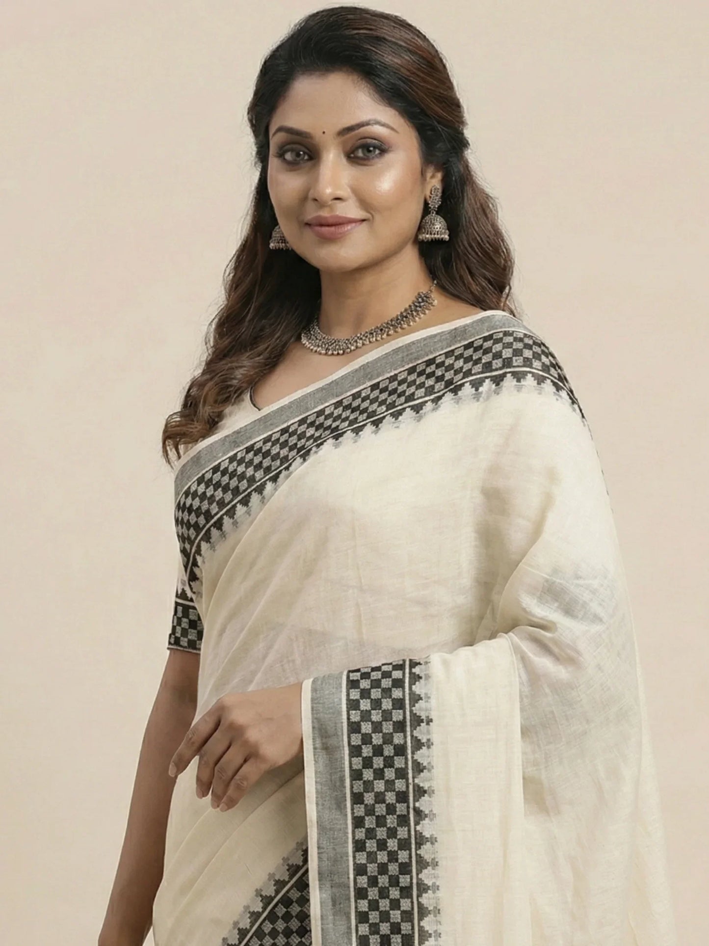 Woman wearing a white saree with black patterns on a beige background

