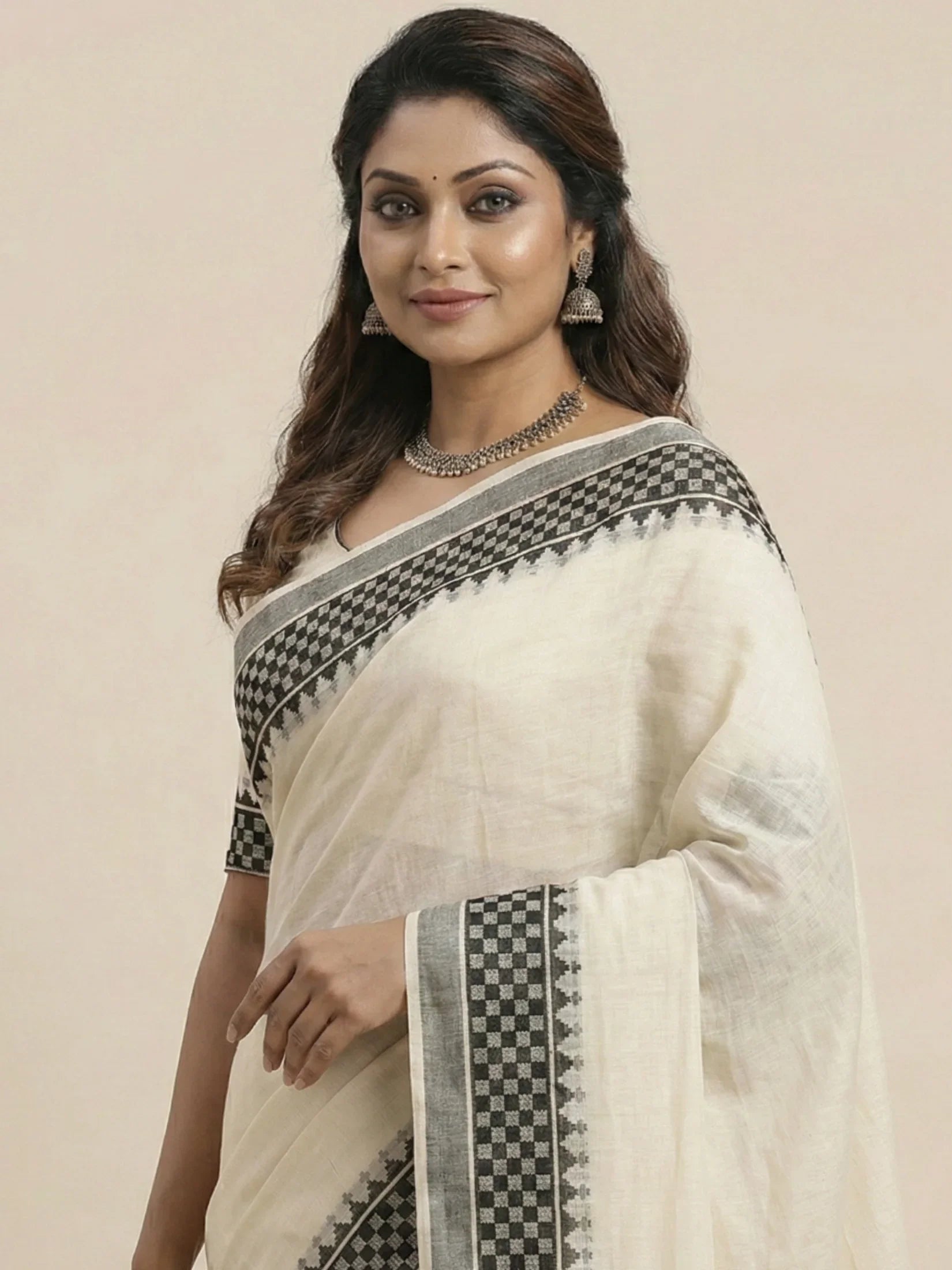 Woman wearing a white saree with black patterns on a beige background
