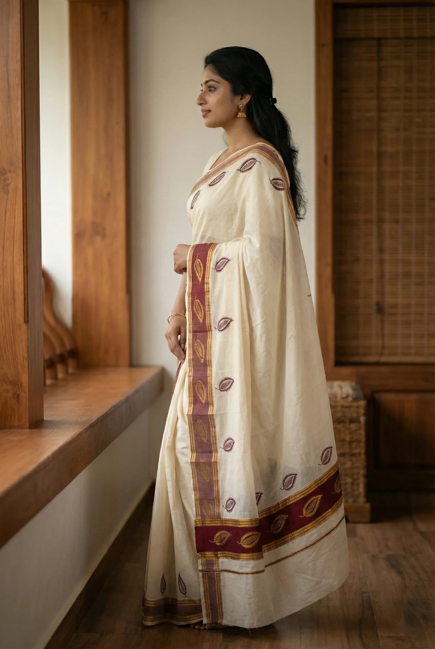 Side view of a woman draped in a Kerala Mundum Neriyathum, highlighting the maroon and gold leaf design on the pleats and pallu