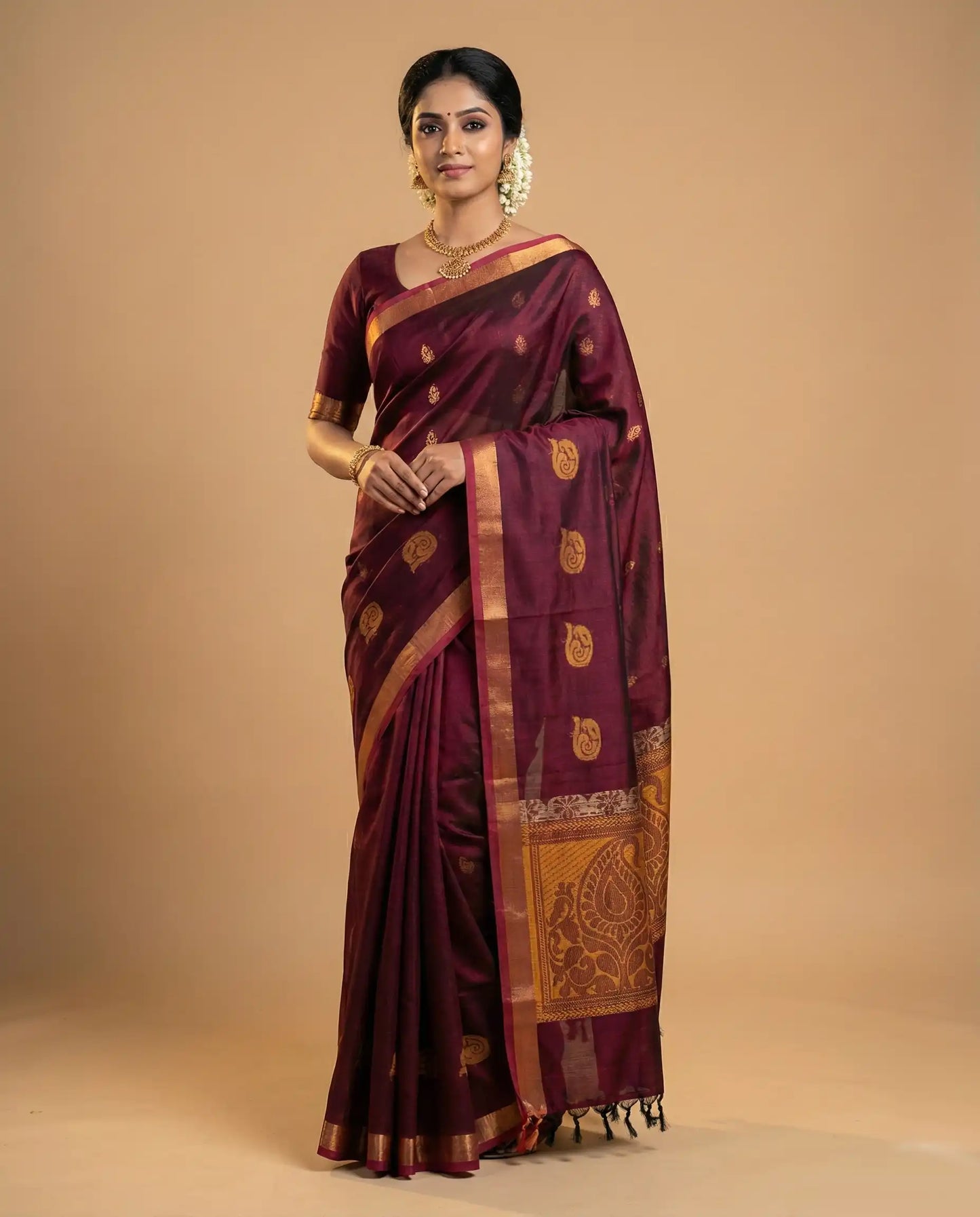 Woman wearing a maroon saree with gold patterns on a beige background

