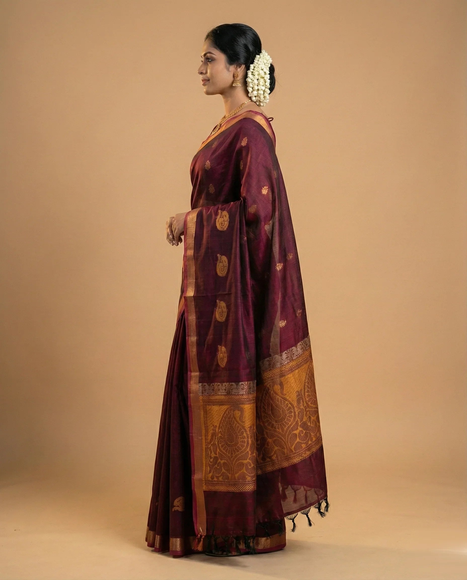 Woman wearing a maroon saree with gold patterns on a beige background

