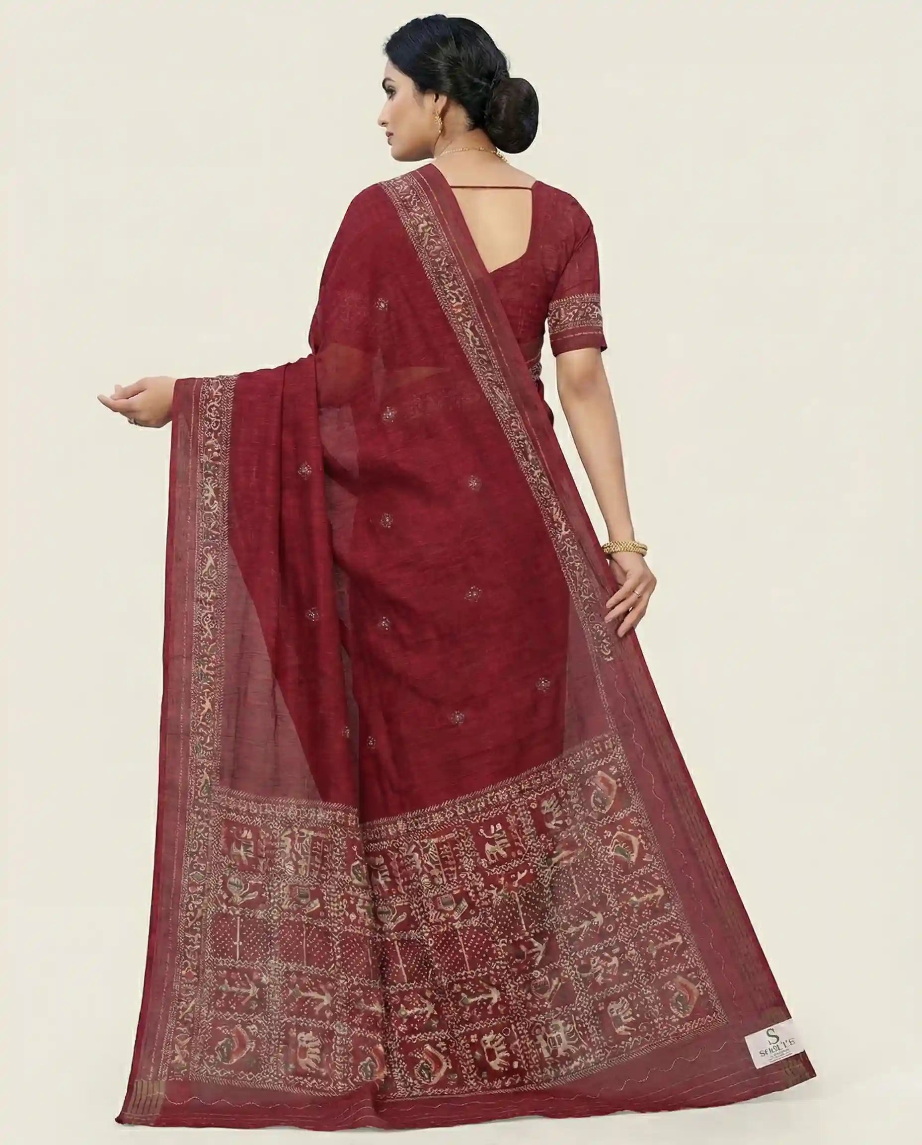 Side profile of a model showcasing the elegant drape and texture of a maroon traditional saree from Sherly's Attire.