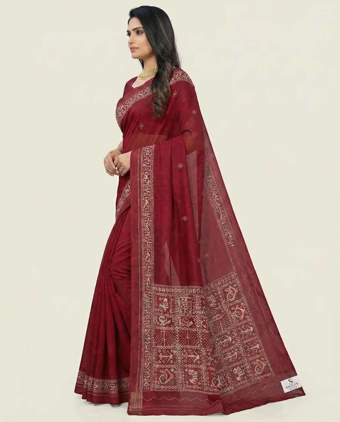 Side profile of a model showcasing the elegant drape and texture of a maroon traditional saree from Sherly's Attire.