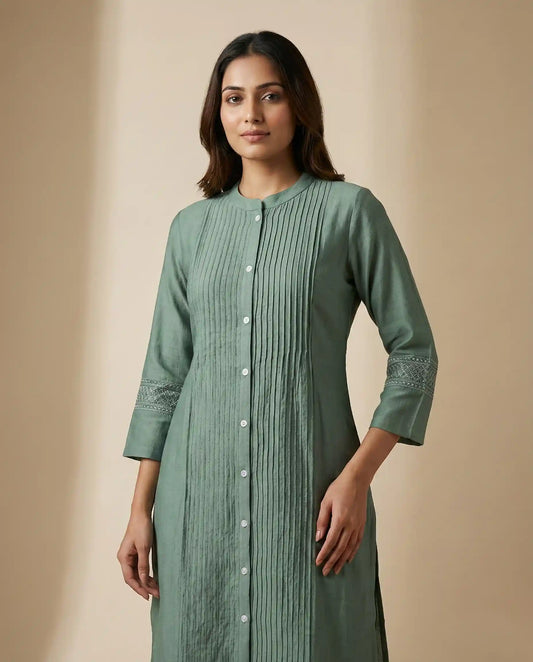 Woman wearing a green pleated dress against a beige background

