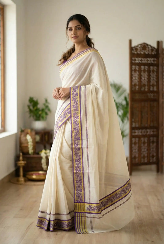 Woman wearing a traditional white saree with purple and gold border in a room.

