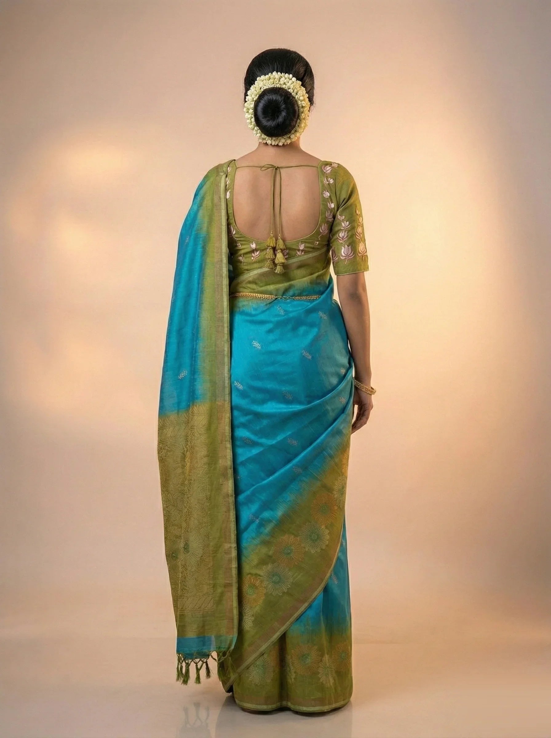 Woman wearing a green and blue saree with a plain background

