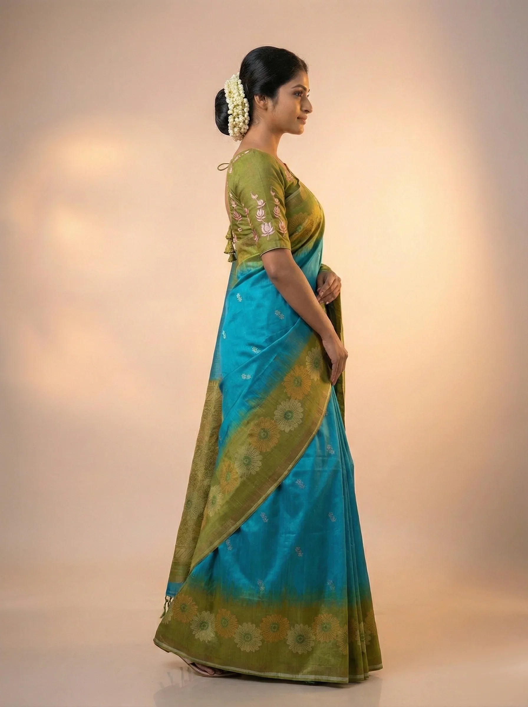 Woman wearing a green and blue saree with a plain background

