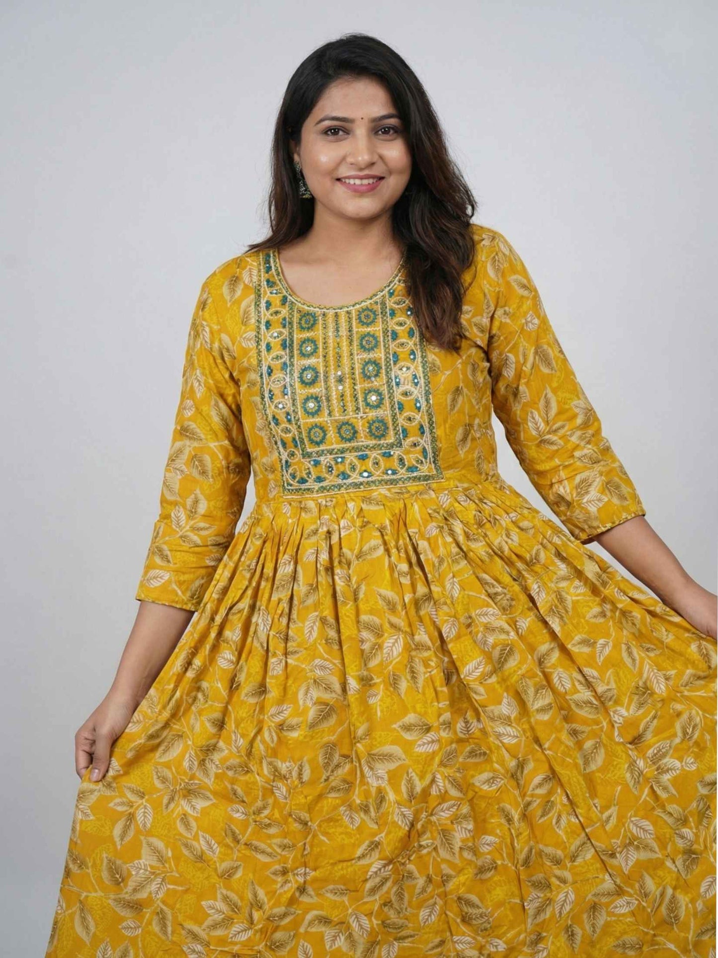 Woman wearing a yellow patterned dress against a plain background
